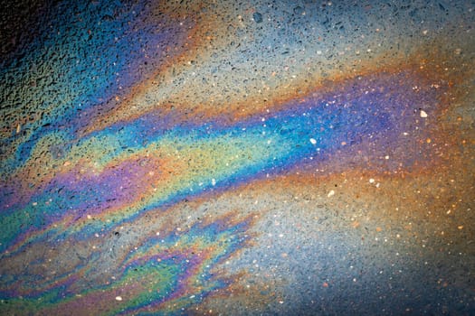 Oil stain on the asphalt, rainbow-shaped colored gasoline stains on an asphalt road as a texture or background. Oil petrol water pollution.