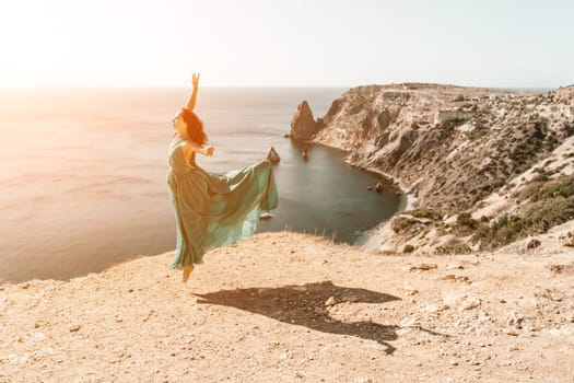 Woman green dress sea. Female dancer posing on a rocky outcrop high above the sea. Girl on the nature on blue sky background. Fashion photo