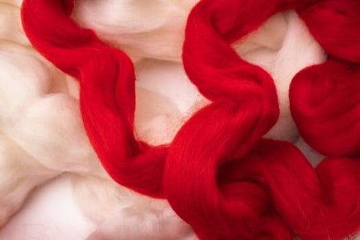 White and red merino wool for felting folded in an abstract pattern as texture and background.