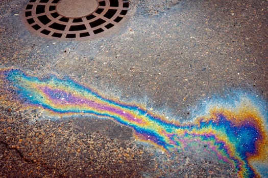 Oil slick on the asphalt road background drains into the storm drain. Abstract background from motor oil, gas or petrol spilled on asphalt.