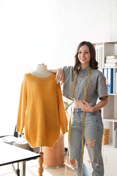 Female fashion designer are designing new trendy clothing collection. young beautiful woman tailor leaning on clothes rack.