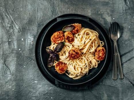 Meatballs Pasta Carbonara in black craft plate over gray background. Close up view of creamy carbonara with copy space. Comfort food concept. Top view or flat lay.
