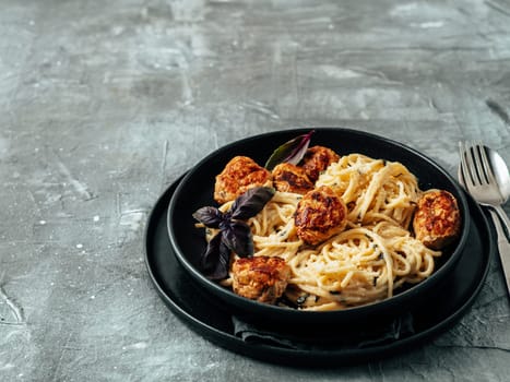 Meatballs Pasta Carbonara in black craft plate over gray background. Close up view of creamy carbonara pasta with meatballs with copy space. Comfort food concept