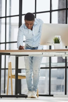 Serious thoughtful millennial businessman standing leaning on desk