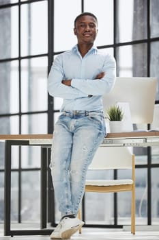 african american man sitting on a table and posing with folded hands in his office