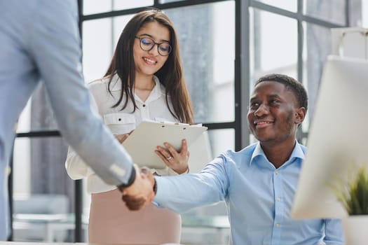Cheerful multiracial colleagues discussing startup project and smiling during workday in office interior