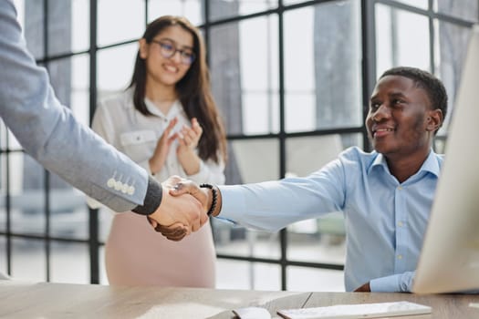 Cheerful multiracial colleagues discussing startup project and smiling during workday in office interior