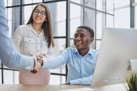 Cheerful multiracial colleagues discussing startup project and smiling during workday in office interior