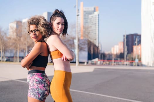 portrait of two female runners standing looking at camera with arms crossed in the city, concept of friendship and sportive lifestyle, copy space for text