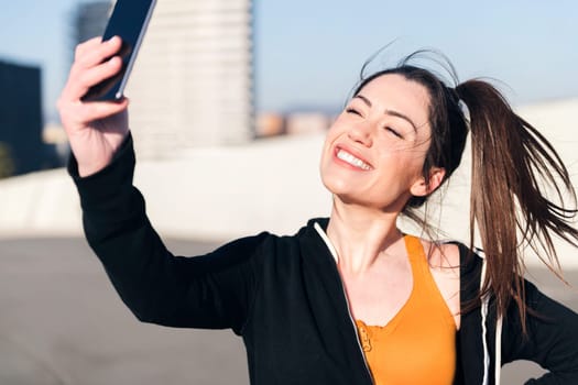 beautiful female runner taking a selfie with mobile phone in the street, concept of social media and sportive lifestyle