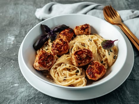 Meatballs Pasta Carbonara in white plate over gray background. Close up view of creamy carbonara pasta with meatballs with copy space left. Comfort food concept