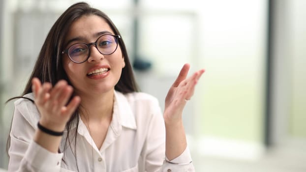 Close-up portrait of a confident and attractive woman in a white blouse and glasses in a classroom or office.