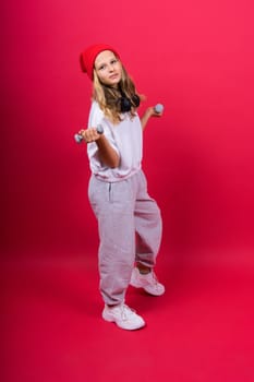 Kid girl doing fitness exercises with dumbbells on a red background