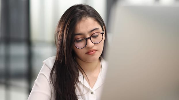 Beautiful portrait of a young woman and female student, while working on her computer or laptop at the office table.