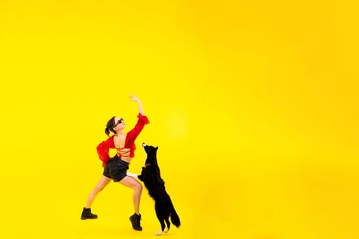 Excited girl dancing with border collie. Studio portrait lady looking at a dog with surprised smile.