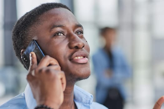 young Afro-American man walking through lobby of busy office building, talking on smartphon