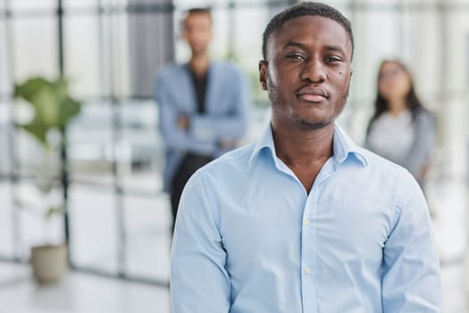 African American businessman in a blue shirt looking at the camera against the background of colleagues