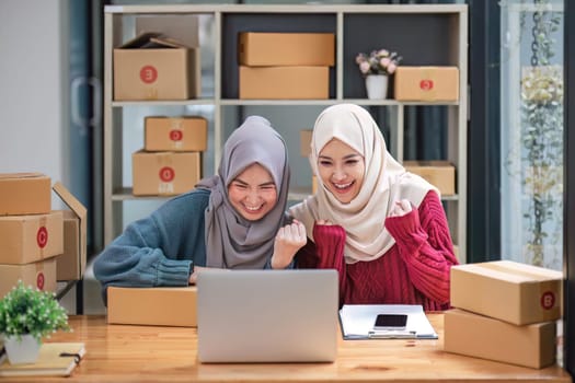 Friend muslim female two work business sme online shopping working on laptop computer with parcel box on desk at home, SME online business