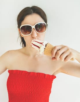 Cinematic photo filter. Happy cheerful girl in a red top and white sunglasses eats a colorful ice cream cone in her hands and smiles