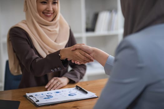 A beautiful and cheerful Asian Muslim businesswoman shaking hands with a female business partner during the meeting in the office...