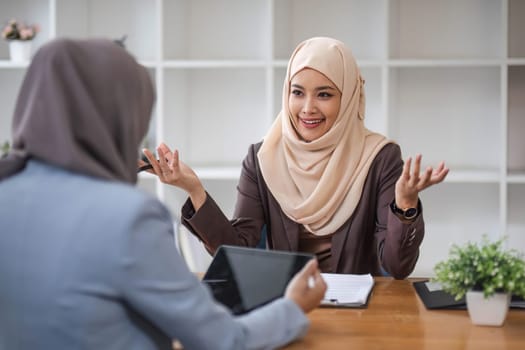 A professional and confident Asian Muslim businesswoman discussing work with her colleague in the office...