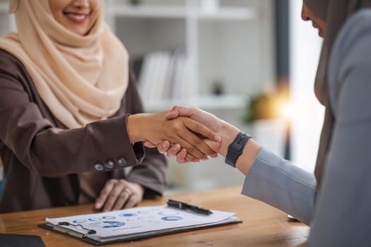 A beautiful and cheerful Asian Muslim businesswoman shaking hands with a female business partner during the meeting in the office...