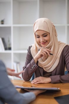 A professional and confident Asian Muslim businesswoman discussing work with her colleague in the office...