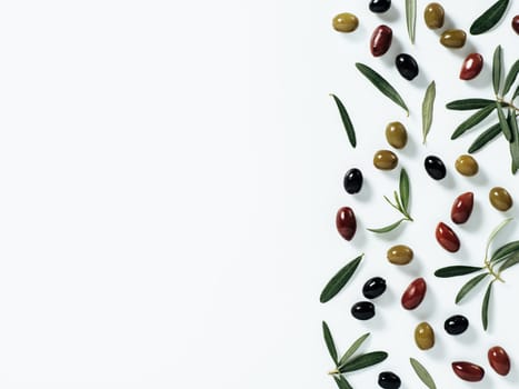 Pattern with green, black and red olives and olives tree leaves and branches on white background. Mix olive tree fruits and branches as background with copy space. Top view or flat lay.