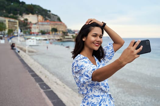 Beautiful smiling young woman takes selfie with a smartphone at the Promenade des Anglais in Nice, France