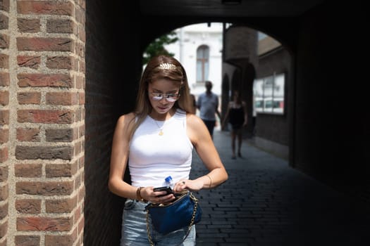 a young woman is nervously looking for something in her handbag against the background of a dark arch in a brick house,beautiful stylish clothes and gold accessories, High quality photo