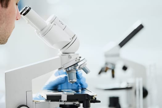 selective focus of male scientist looking through microscope in laboratory