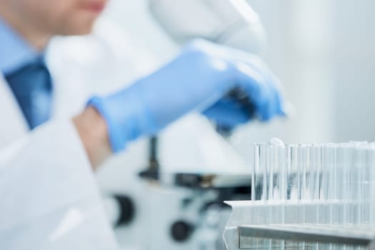 selective focus of male scientist looking through microscope in laboratory