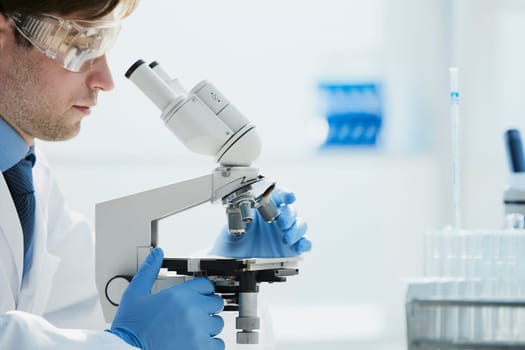 selective focus of male scientist looking through microscope in laboratory