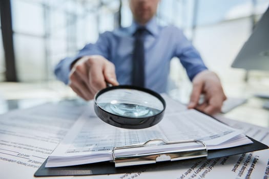 man looking through a magnifying glass to documents notebook.