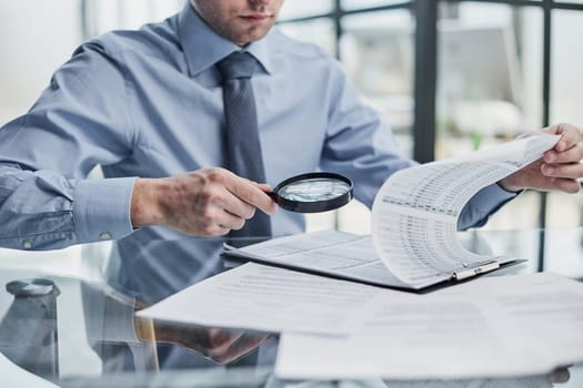 man looking through a magnifying glass to documents notebook.