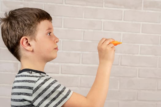 A happy Caucasian boy of school age writes in the air with an orange marker. The concept of study and school activities and education