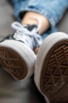 the soles of new youth sneakers with lacing worn on a girl lying on a home sofa. Trends of fashionable everyday concept.