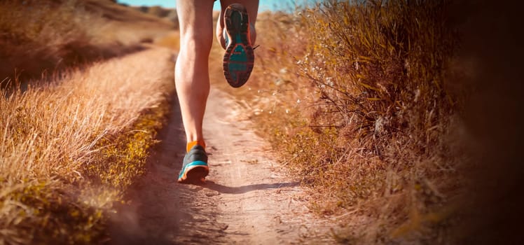 Athlete runner legs running on a close-up of a trail across a field on a shoe. Fitness and warm-up, young man with sun effect in the background.