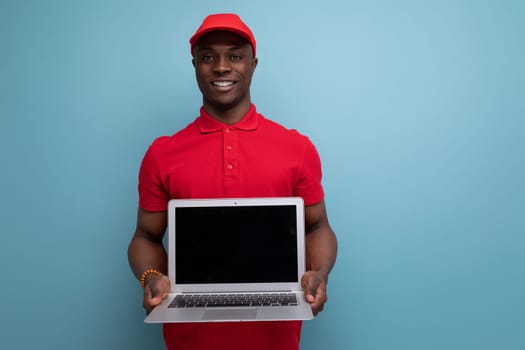 young delivery worker american man in red rendered t-shirt and caps showing advertisement on laptop with mockup.