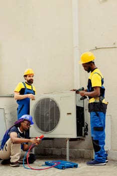 Qualified electricians installing condenser for client after replacing broken unit. Professional workers enlisted to optimize new HVAC system's performance, ensuring it operates at maximum capacity