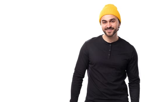 young brutal male model dressed in a black jacket and a yellow hat is smiling on a white background with copy space.