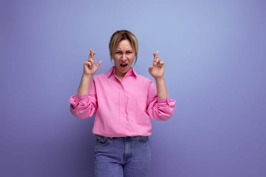 pretty young blond european woman model wearing pink shirt and jeans crossed her fingers and hopes for good luck.