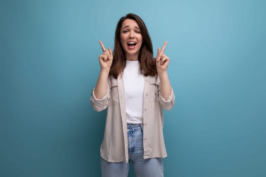 ecstatic 30s dark haired woman in beige shirt on blue background.