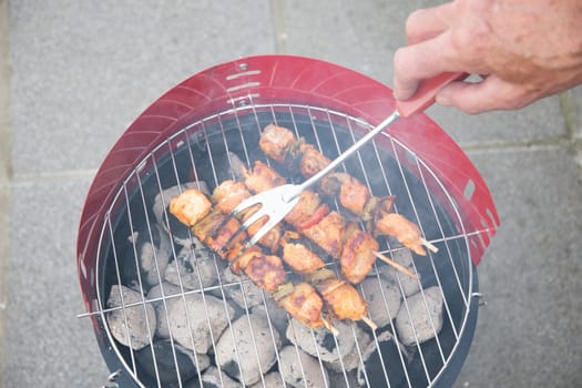 man flipping chicken skewers on barbecue grill over hot coals, summer delicacies, vacation food on terrace. High quality photo
