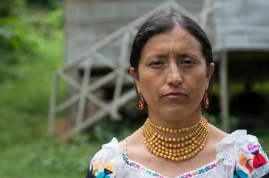 native older woman with a serious face, dressed in traditional indigenous dress next to her house in the Amazon. High quality photo