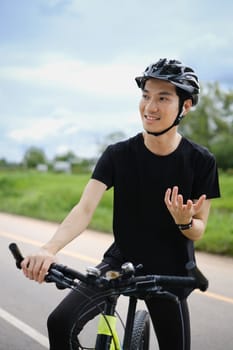 Happy asian man cyclist speaking on phone through earphones while having break during cycling bike in the park.