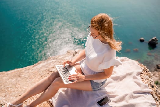 Freelance woman working on a laptop by the sea, typing away on the keyboard while enjoying the beautiful view, highlighting the idea of remote work