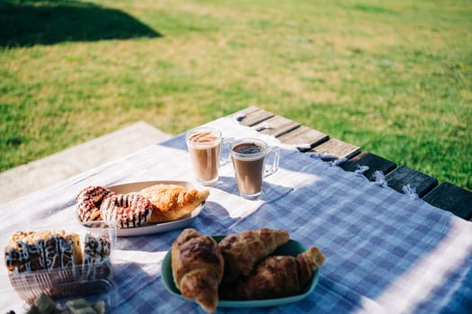 A picnic at the green lawn in the park. Closeup picture of breakfast with coffee, croissants and donuts on green grass outdoors meadow