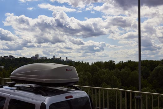 Photo of car with roof rack rides on bridge over river against blue sky.