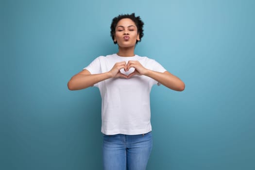 well-groomed beautiful young swarthy woman with fluffy curly hair dressed in a white t-shirt on a blue background with copy space.